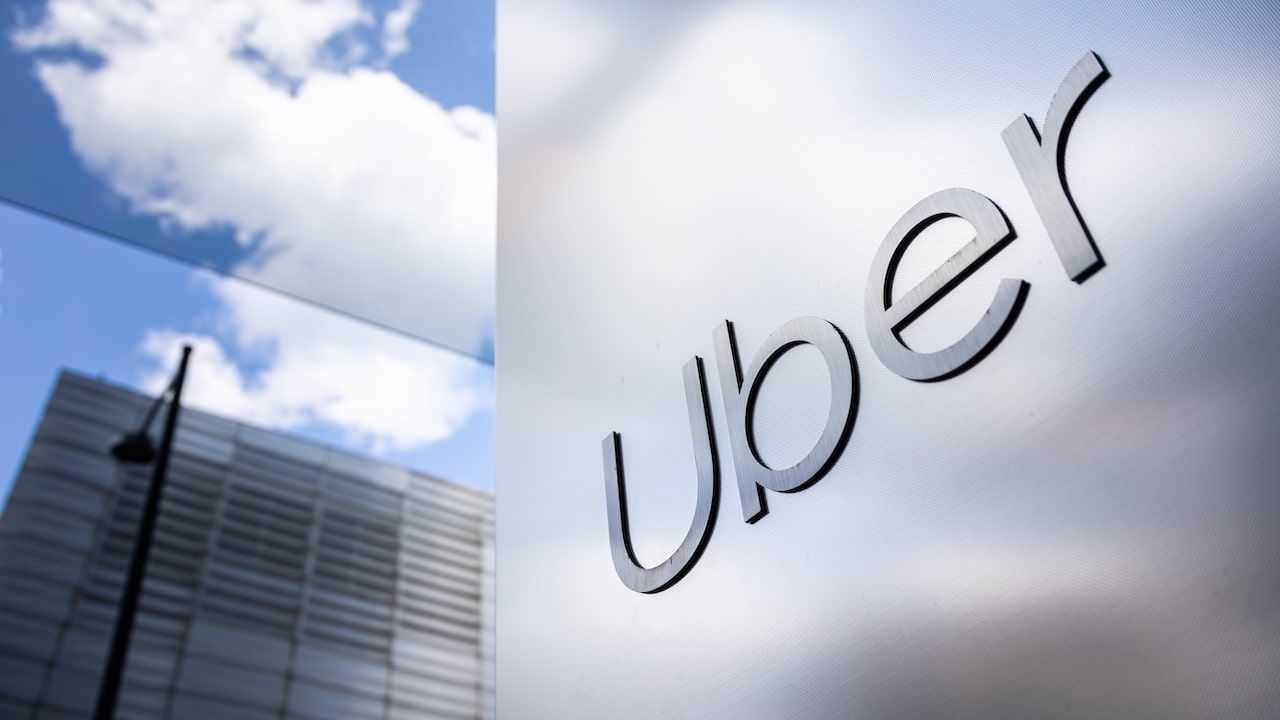 Uber logo on a sleek, reflective wall with urban high-rises in the background, representing modern transportation and technology innovation. Uber headquarters offices