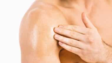 Muscular man applying testosterone gel on shoulder