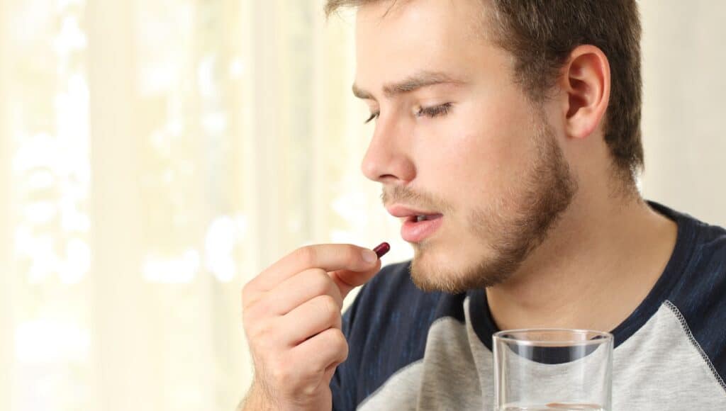 man taking a pill standing at home