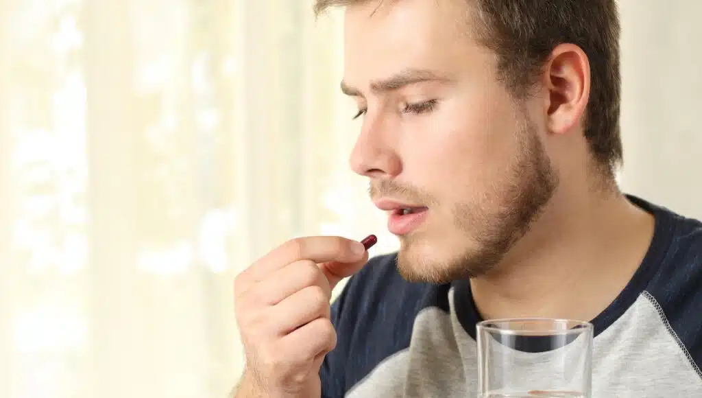 man taking a pill standing at home