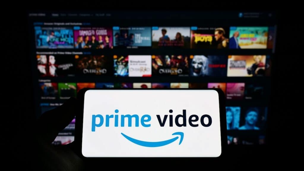 Person holding smartphone with logo of streaming service Amazon Prime Video on screen in front of website. Focus on phone display. Unmodified photo.