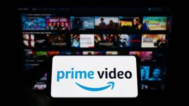 Person holding smartphone with logo of streaming service Amazon Prime Video on screen in front of website. Focus on phone display. Unmodified photo.