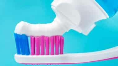 Close up macro of toothpaste squeezed tube putting paste on toothbrush.