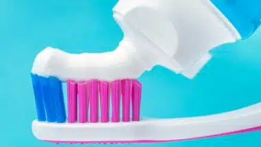 Close up macro of toothpaste squeezed tube putting paste on toothbrush.