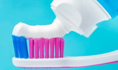 Close up macro of toothpaste squeezed tube putting paste on toothbrush.