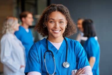 Confident happy woman nurse smiling with crossed arms with healthcare team in background.