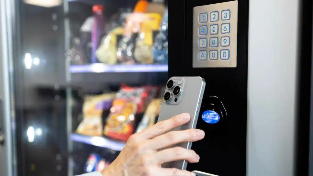 Businesswoman buying snacks on vending machine and making contactless payment via smart phone.