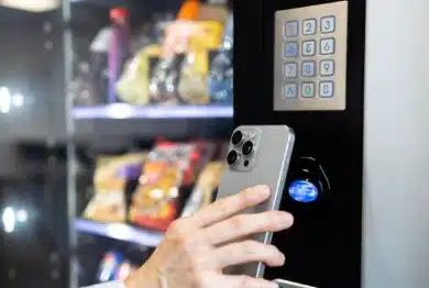 Businesswoman buying snacks on vending machine and making contactless payment via smart phone.
