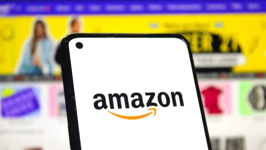 Amazon logo on phone screen with online shopping page background.