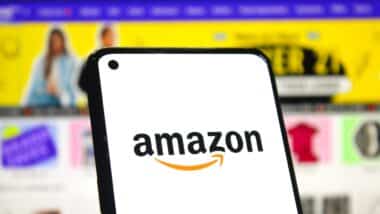 Amazon logo on phone screen with online shopping page background.