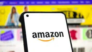 Amazon logo on phone screen with online shopping page background.