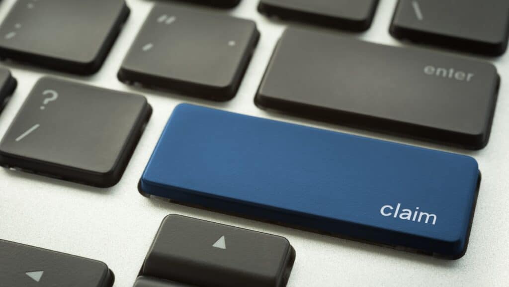 Close up laptop keyboard focus on a blue button with typographic word CLAIM for business and insurance concepts.