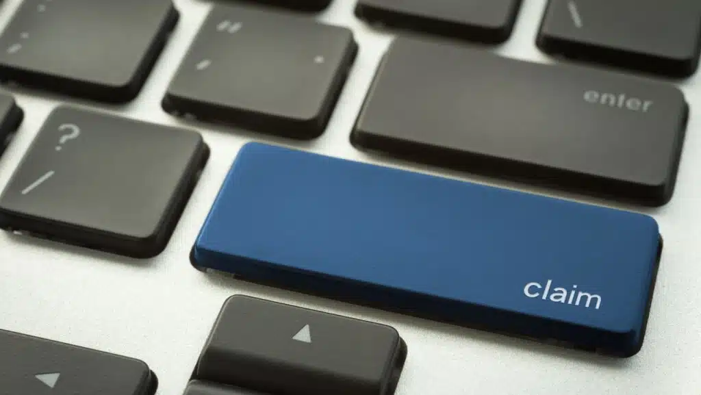 Close up laptop keyboard focus on a blue button with typographic word CLAIM for business and insurance concepts.