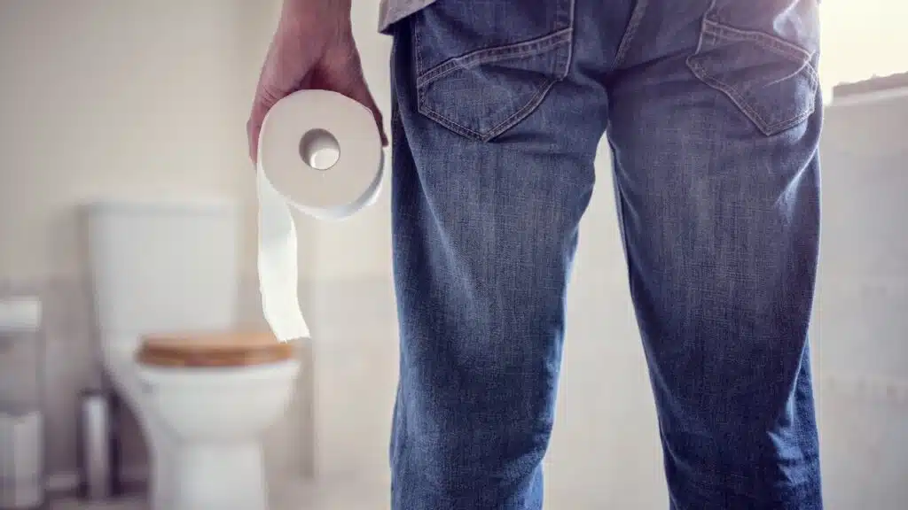 Man holding toilet tissue roll in bathroom looking at loo