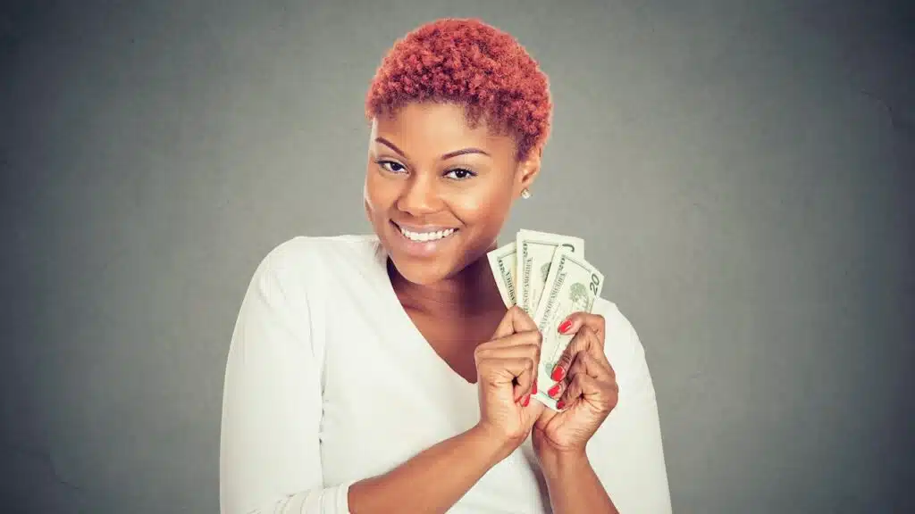 Portrait of super happy excited successful young woman holding money dollar bills in hand, isolated on gray background.