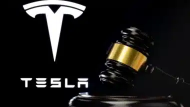 Judge's gavel in front and blurred Tesla Company logo seen on screen behind.