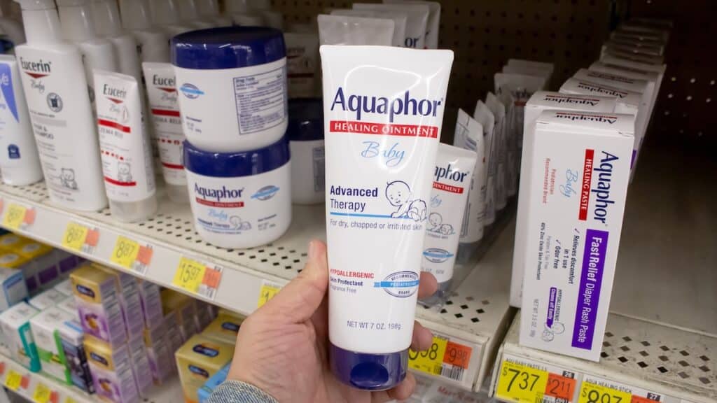 A view of a hand holding a container of Aquaphor baby healing ointment, on display at a local retail store.