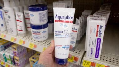 A view of a hand holding a container of Aquaphor baby healing ointment, on display at a local retail store.