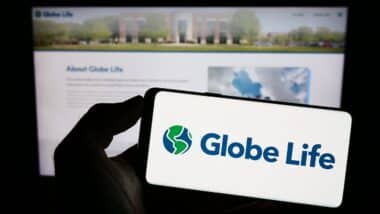 Person holding cellphone with logo of US insurance company Globe Life Inc. on screen in front of business webpage.