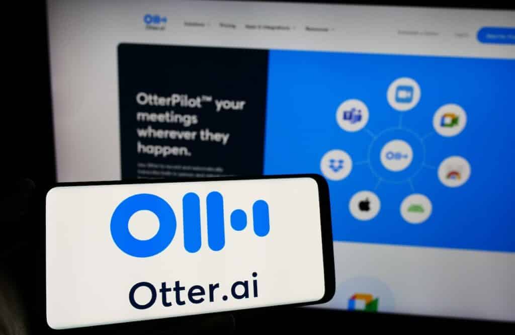 Person holding mobile phone with logo of American artificial intelligence company Otter.ai Inc. in front of web page.