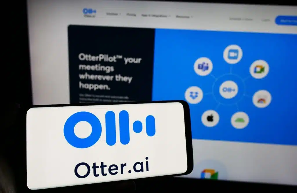 Person holding mobile phone with logo of American artificial intelligence company Otter.ai Inc. in front of web page.