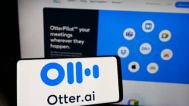 Person holding mobile phone with logo of American artificial intelligence company Otter.ai Inc. in front of web page.