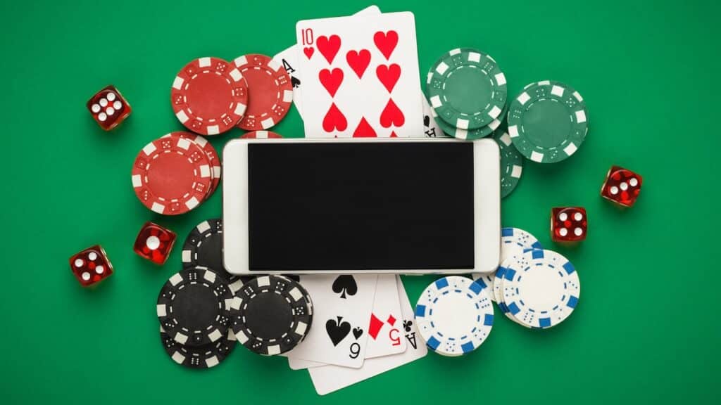 online casino concept, playing cards, dice chips and smartphone with copyspace on the green table. view from above.