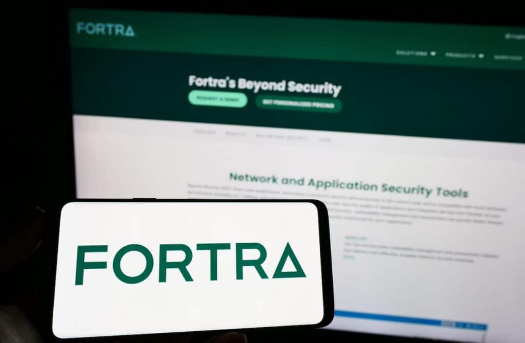 Person holding mobile phone with logo of American cybersecurity company Fortra LLC on screen in front of web page.
