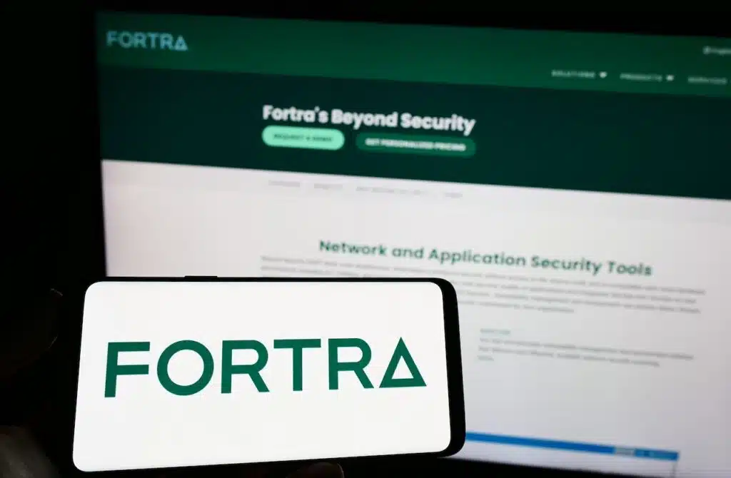 Person holding mobile phone with logo of American cybersecurity company Fortra LLC on screen in front of web page.