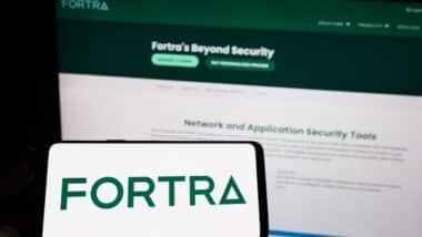 Person holding mobile phone with logo of American cybersecurity company Fortra LLC on screen in front of web page.
