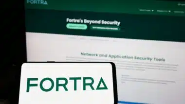 Person holding mobile phone with logo of American cybersecurity company Fortra LLC on screen in front of web page.