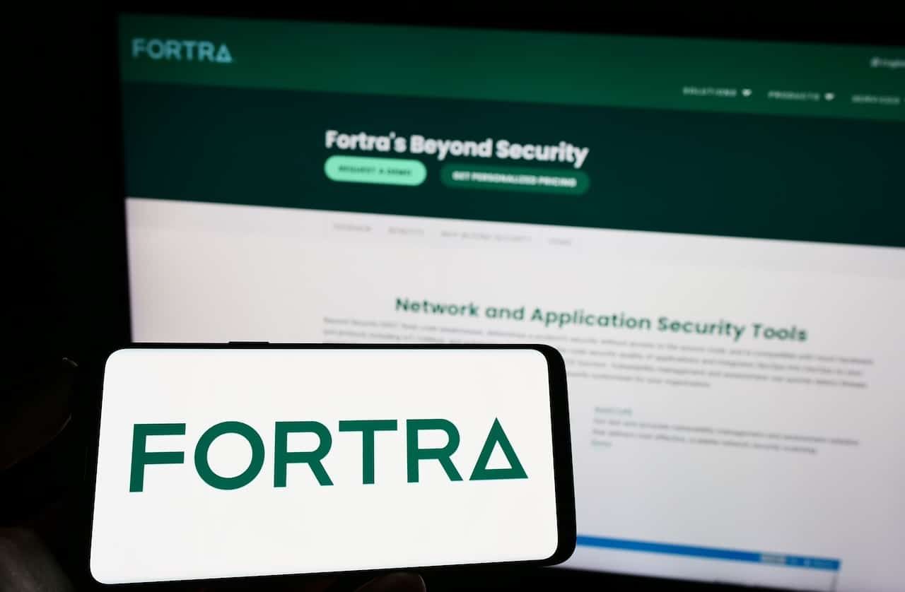 Person holding mobile phone with logo of American cybersecurity company Fortra LLC on screen in front of web page.