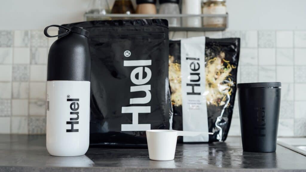 Branded Bags of balanced nutritionally complete meals, shaker and pot from Huel brand on the kitchen table.
