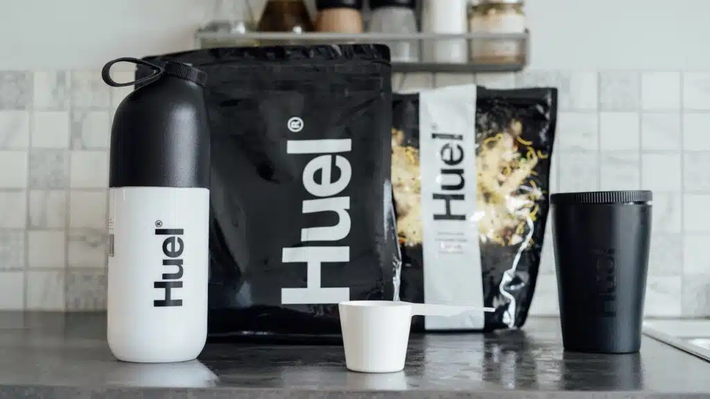 Branded Bags of balanced nutritionally complete meals, shaker and pot from Huel brand on the kitchen table.