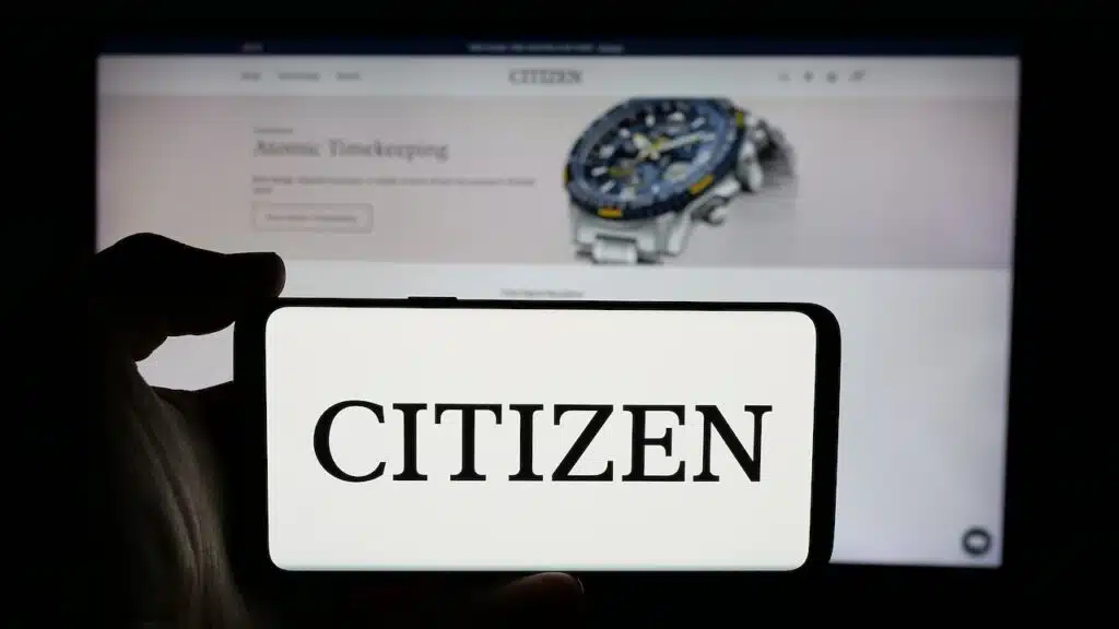 Person holding cellphone with logo of electronics company Citizen Watch Co. Ltd. on screen in front of business webpage.