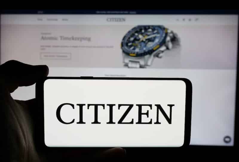 Person holding cellphone with logo of electronics company Citizen Watch Co. Ltd. on screen in front of business webpage.