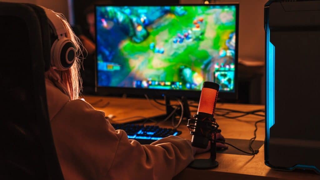 Image from back of caucasian girl playing video game on personal computer while sitting at table indoors