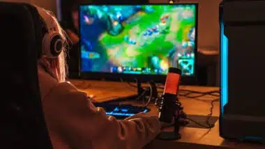 Image from back of caucasian girl playing video game on personal computer while sitting at table indoors