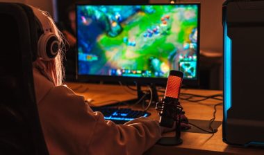 Image from back of caucasian girl playing video game on personal computer while sitting at table indoors