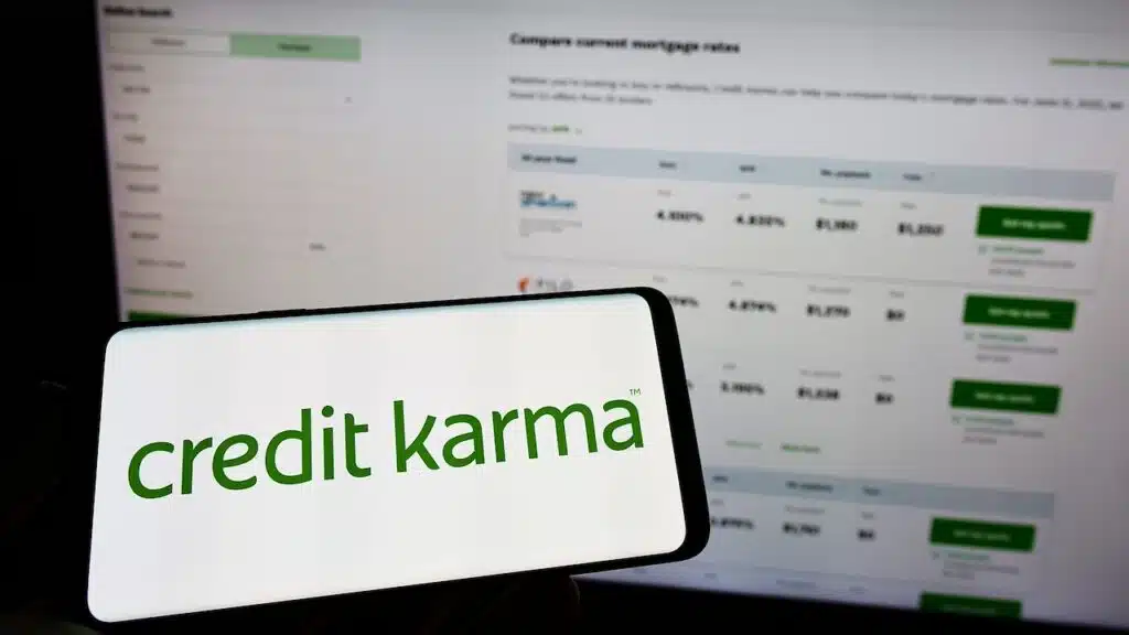 Person holding mobile phone with logo of American financial company Credit Karma Inc. on screen in front of web page.