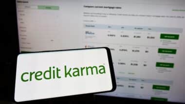 Person holding mobile phone with logo of American financial company Credit Karma Inc. on screen in front of web page.