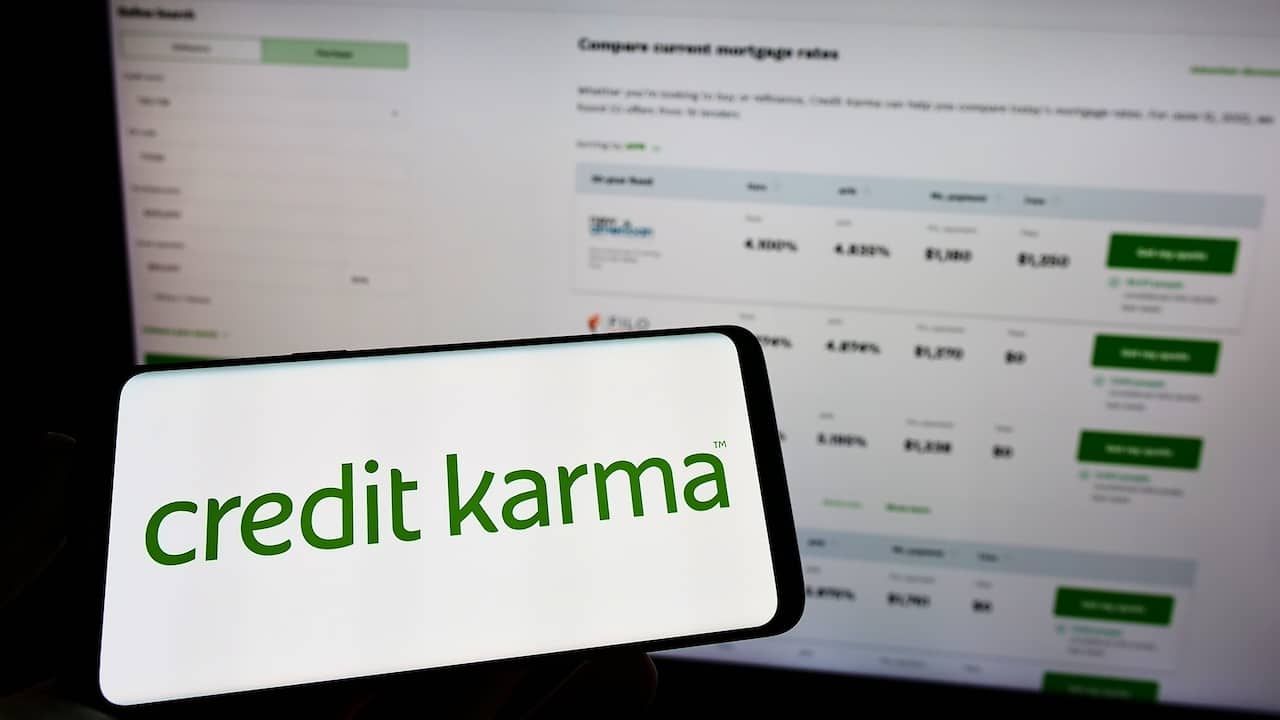 Person holding mobile phone with logo of American financial company Credit Karma Inc. on screen in front of web page.