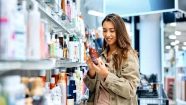 Young happy woman reading ingredients of skin care product while shopping at the store.