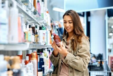 Young happy woman reading ingredients of skin care product while shopping at the store.