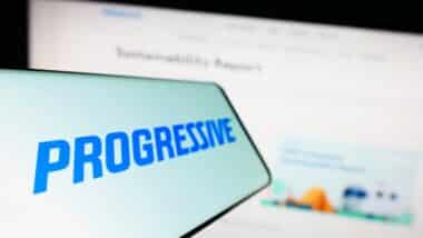 Smartphone with logo of American insurance company The Progressive Corporation on screen in front of website.