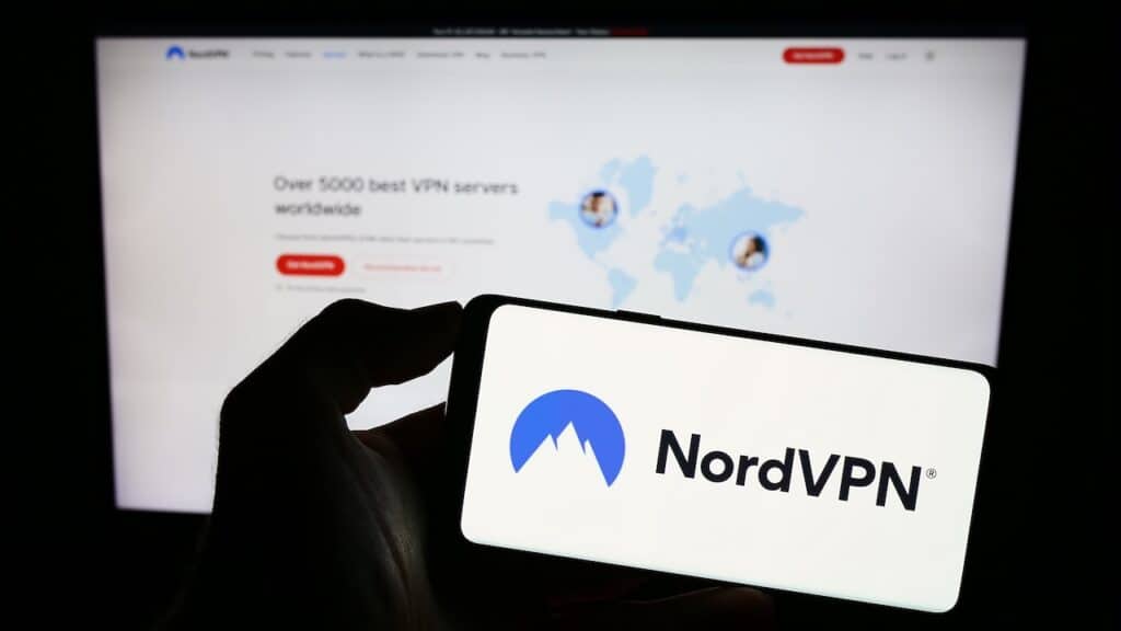Person holding mobile phone with logo of VPN service NordVPN (Nordsec Ltd.) on screen in front of business web page.