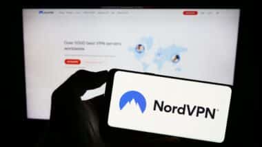 Person holding mobile phone with logo of VPN service NordVPN (Nordsec Ltd.) on screen in front of business web page.