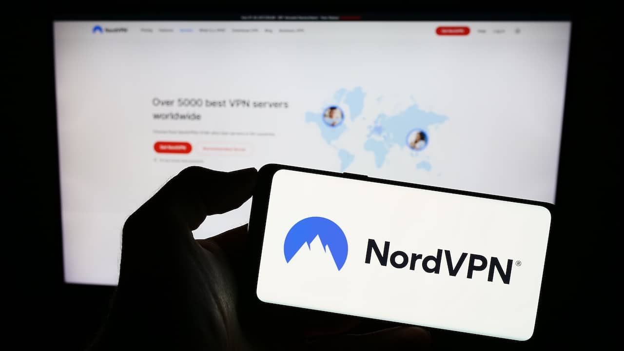 Person holding mobile phone with logo of VPN service NordVPN (Nordsec Ltd.) on screen in front of business web page.