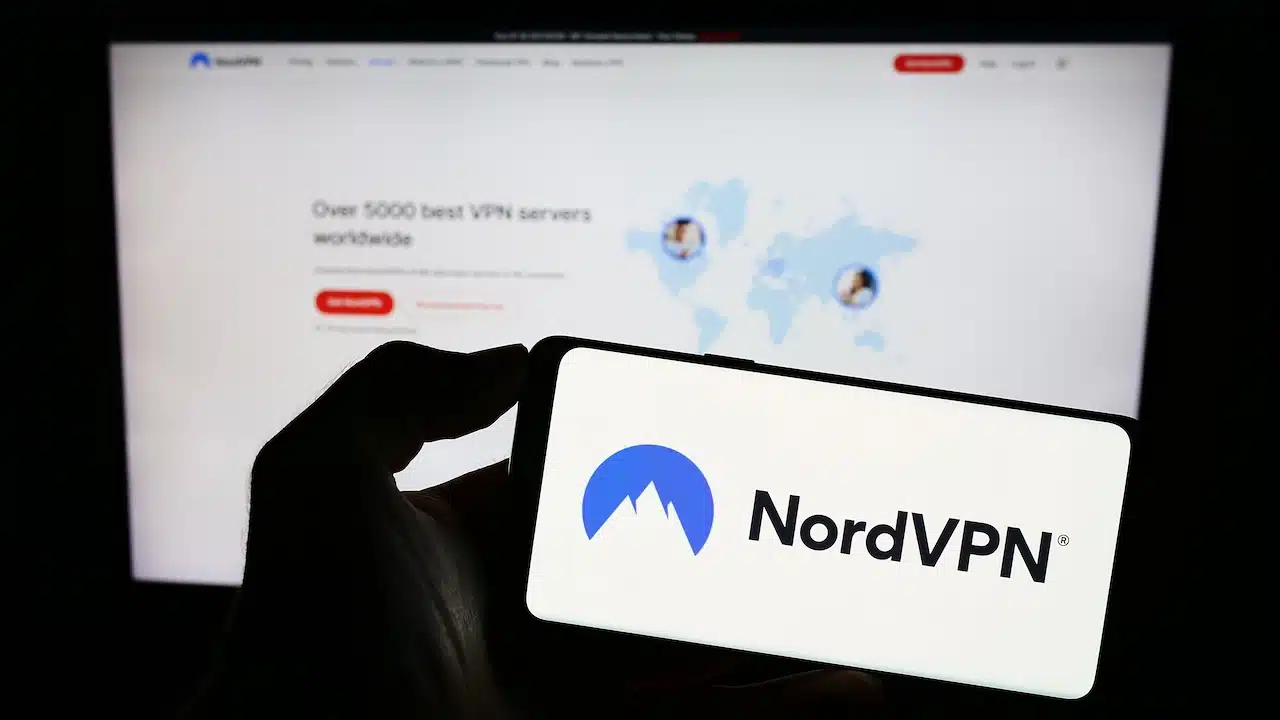 Person holding mobile phone with logo of VPN service NordVPN (Nordsec Ltd.) on screen in front of business web page.