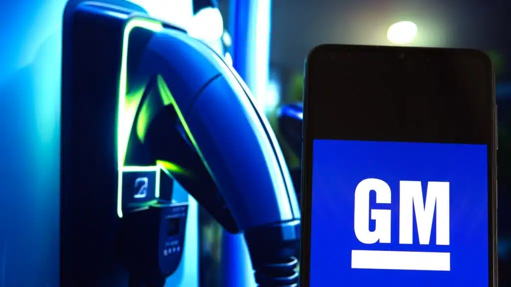 General Motors (GM) logo is displayed on a smartphone screen, close-up view of an electric car charger,